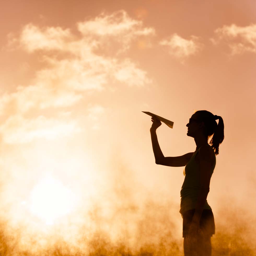 Silhouette of woman throwing paper airplane