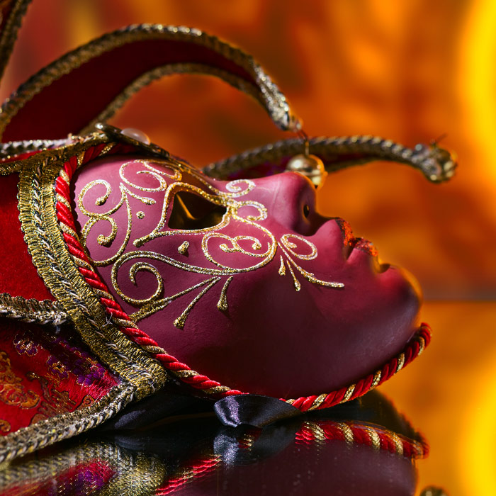 Red and purple theatre mask in front of an orange curtain